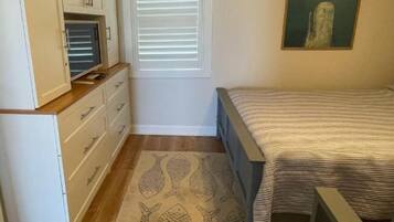 Un dormitorio con cama, cómoda, ventana con persianas y un cuadro en la pared.