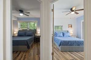 A bedroom with two beds, wooden flooring, ceiling fans, and bedside lamps.