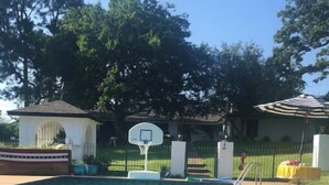 A clear swimming pool with a basketball hoop and a small pavilion.