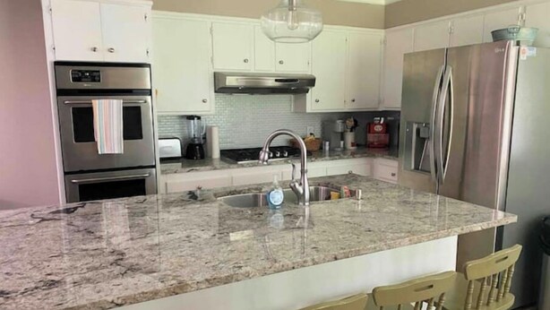 A kitchen with white cabinets, stainless steel appliances, a granite countertop, and a bar stool area.