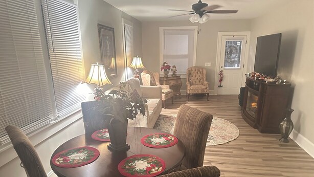 A dining area with a round table, chairs, and a ceiling fan. There are two lamps on the table, a potted plant, and a decorative mirror on the wall.
