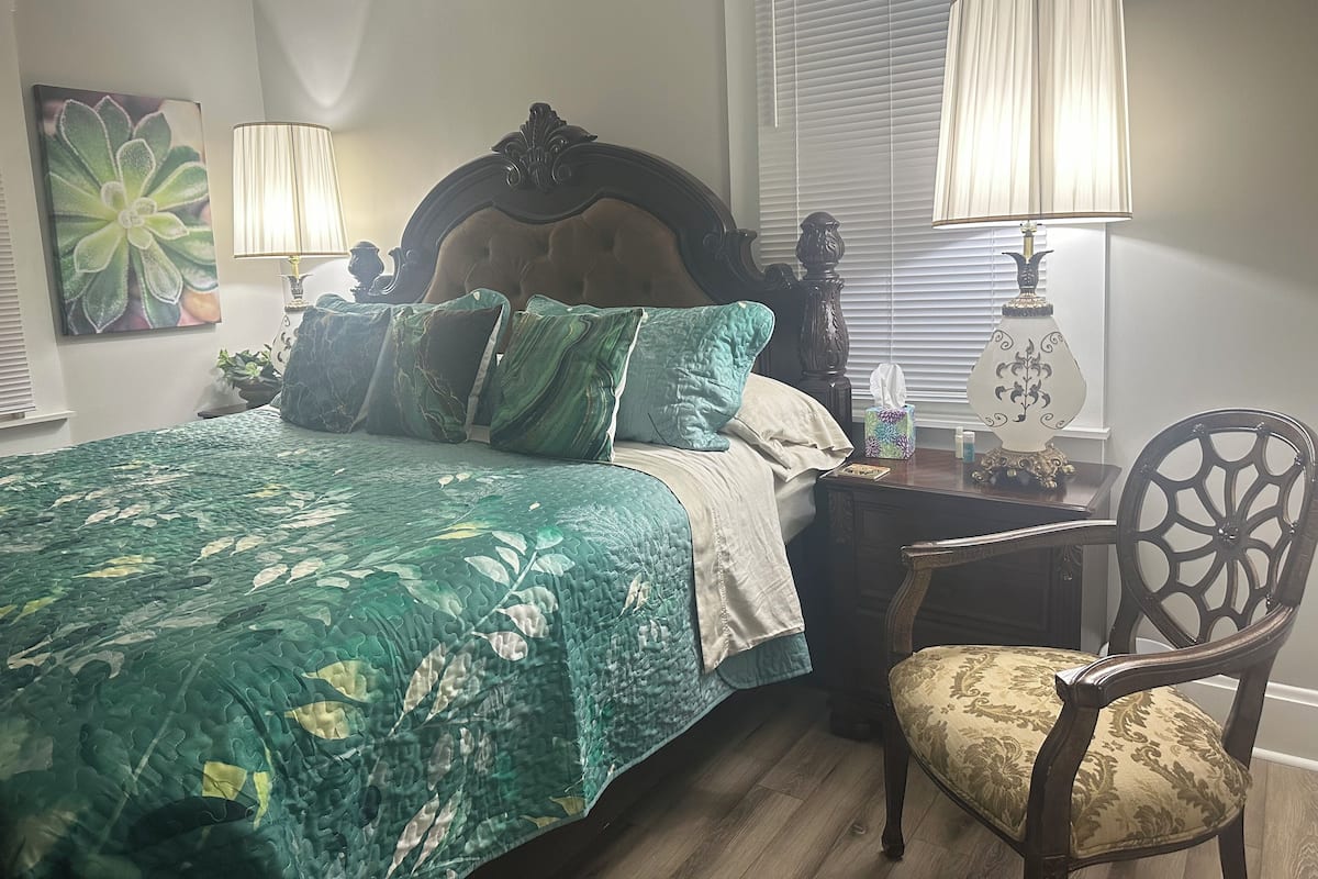 Un dormitorio con una cama, dos lámparas de noche, una silla y una mesita de noche con lámpara.