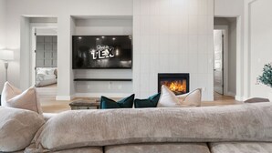 Ein modernes Wohnzimmer mit einem großen Flachbildfernseher, einem Kamin und einem gemütlichen Sofa mit Kissen.