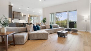 Ein geräumiges Wohnzimmer mit einer großen Eckcouch, einem Couchtisch und einem Essbereich, im Hintergrund ist eine Küche zu sehen.