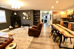 Un salon spacieux doté d’une cheminée, d’un canapé en cuir et d’un coin repas avec une longue table et des chaises en bois.