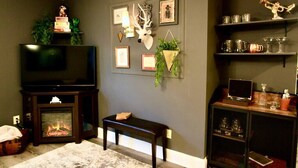 A living room with a fireplace, a television, a bench, and shelves with decorative items. -  The Lounge - Downtown Chillicothe (Chillicothe)