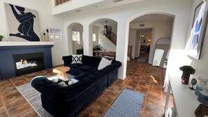 A spacious living area with a dark blue sofa, a small wooden table, and a fireplace. There are multiple archways leading to other rooms. - OCEANSIDE BEACH HOUSE~Dreamy Palm Tree Lined Street~5 MIN WALK to EVERYTHING!  (Oceanside)