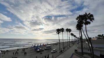 A beachside promenade with palm trees, a road, and beachgoers.