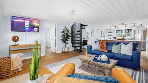A modern living room with a flat-screen TV, a blue sofa, a coffee table, and a staircase leading to the kitchen. - SY Oceanfront-Heated Pool-Bar-firepit-horseshoe (North Myrtle Beach)