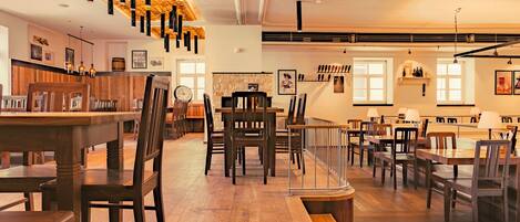 A spacious restaurant with wooden furniture, pendant lighting, and a stone wall.