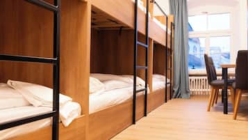 A dormitory room with bunk beds, a wooden desk, and a chair.