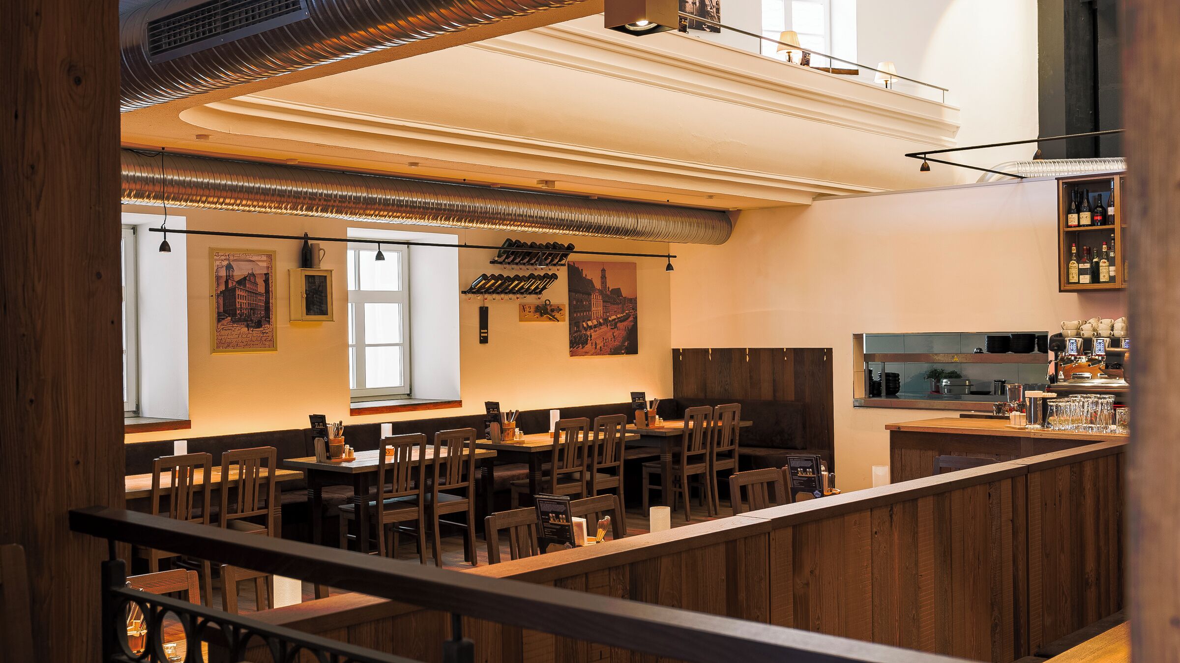 A restaurant with wooden furniture, a bar area, and a view of the city through large windows.