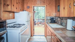 A wooden cabin kitchen with a gas stove, refrigerator, and a view of a deck and outdoor seating area. - Get Cozy on Rainbow, 1 Night Free! (Big Bear City)