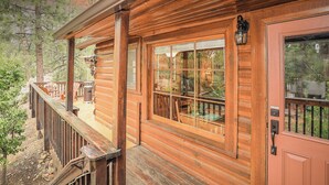 A wooden cabin with a porch, a window with a view of the surrounding forest, and a door with a mailbox. - Get Cozy on Rainbow, 1 Night Free! (Big Bear City)