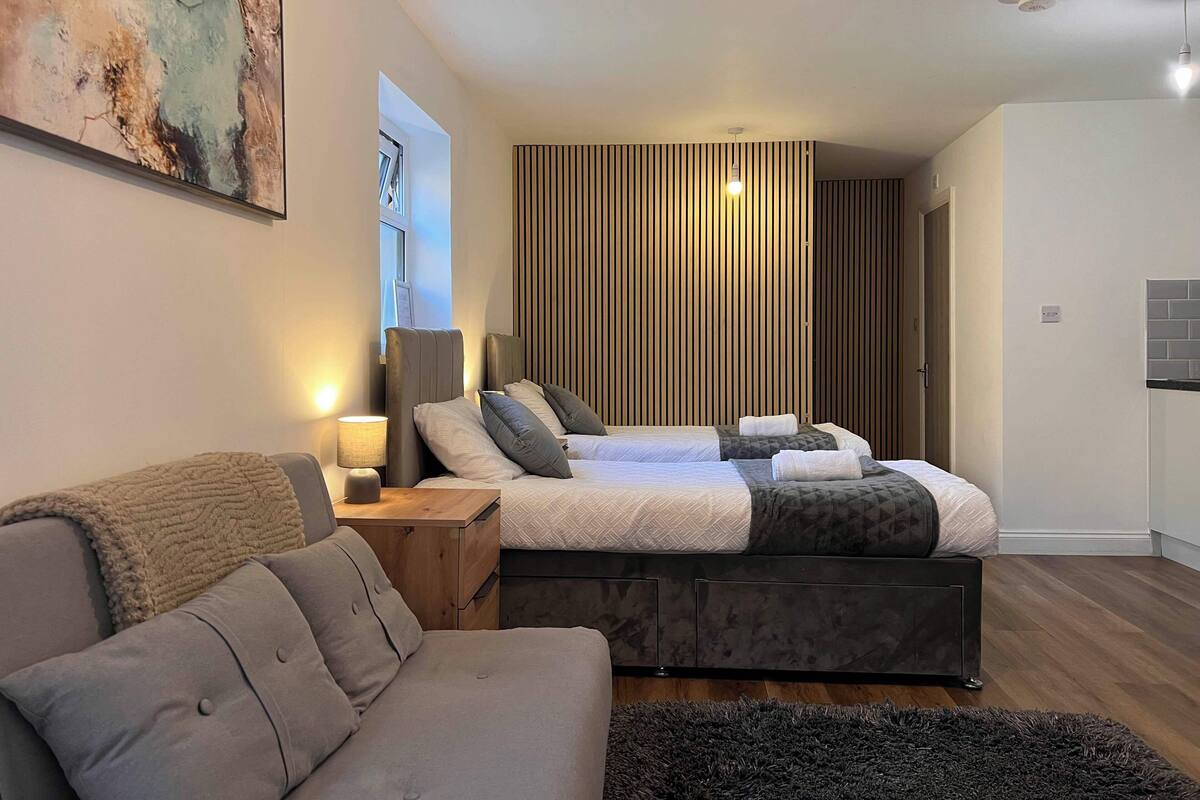 A modern bedroom with a large bed, a sofa, and a wooden floor.