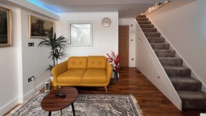 A living room with a mustard sofa, a coffee table, a patterned rug, a staircase, and a door leading to another room. - Haven Homes (Luton)