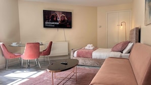 A modern living room with a sofa, a coffee table, a TV mounted on the wall, and a dining area with chairs and a table. - Haven Homes (Luton)