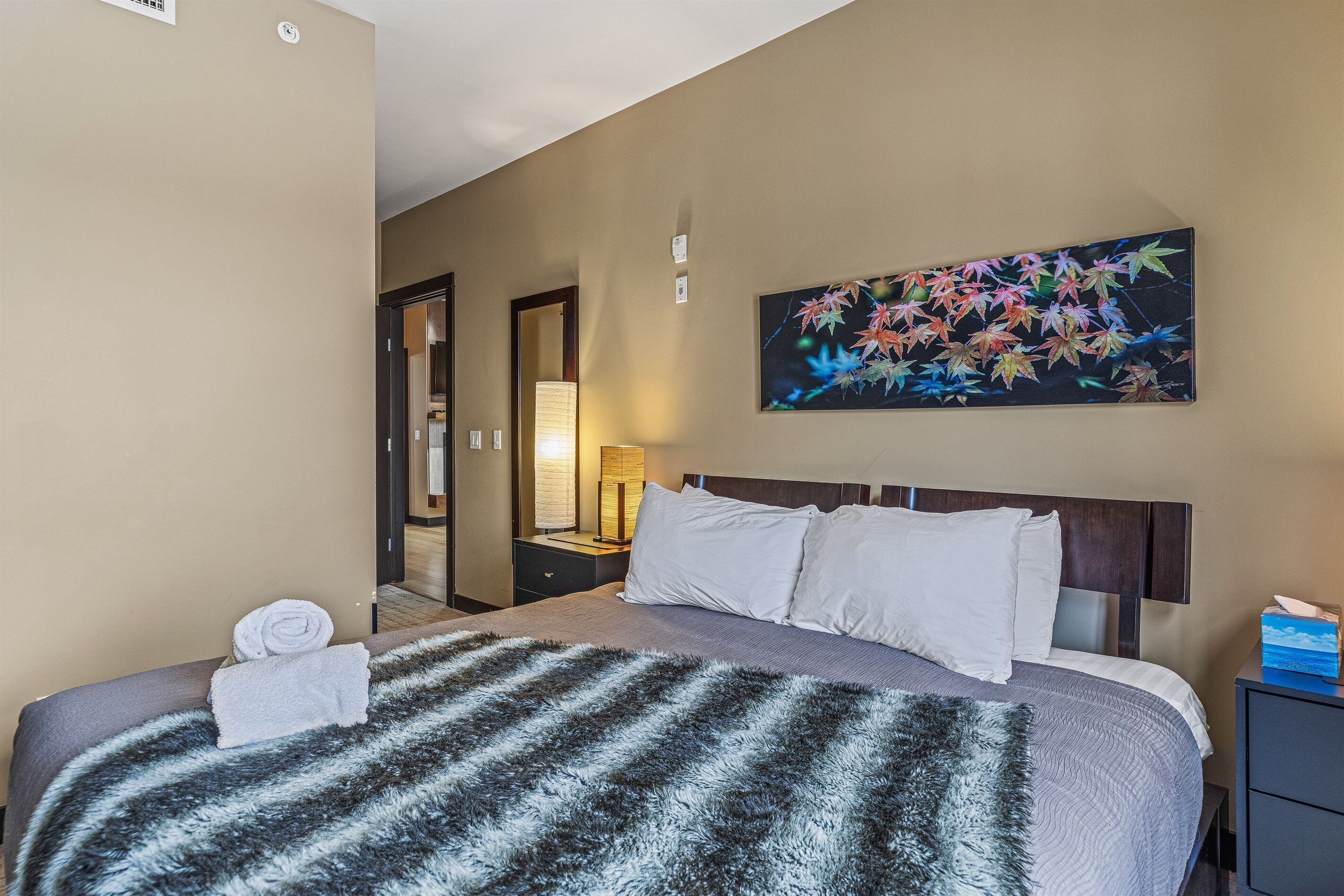 Une chambre d’hôtel avec un lit, un tableau, une table de chevet et une lampe.
