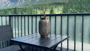 Een balkon met een tafel, stoelen, een decoratieve vaas en uitzicht op de bergen.