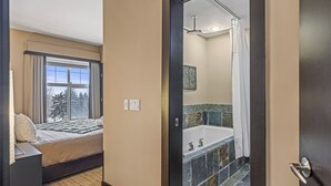Een hotelkamer met een bed, een raam met gordijnen, en een badkamer met een badkuip en betegelde muren.
