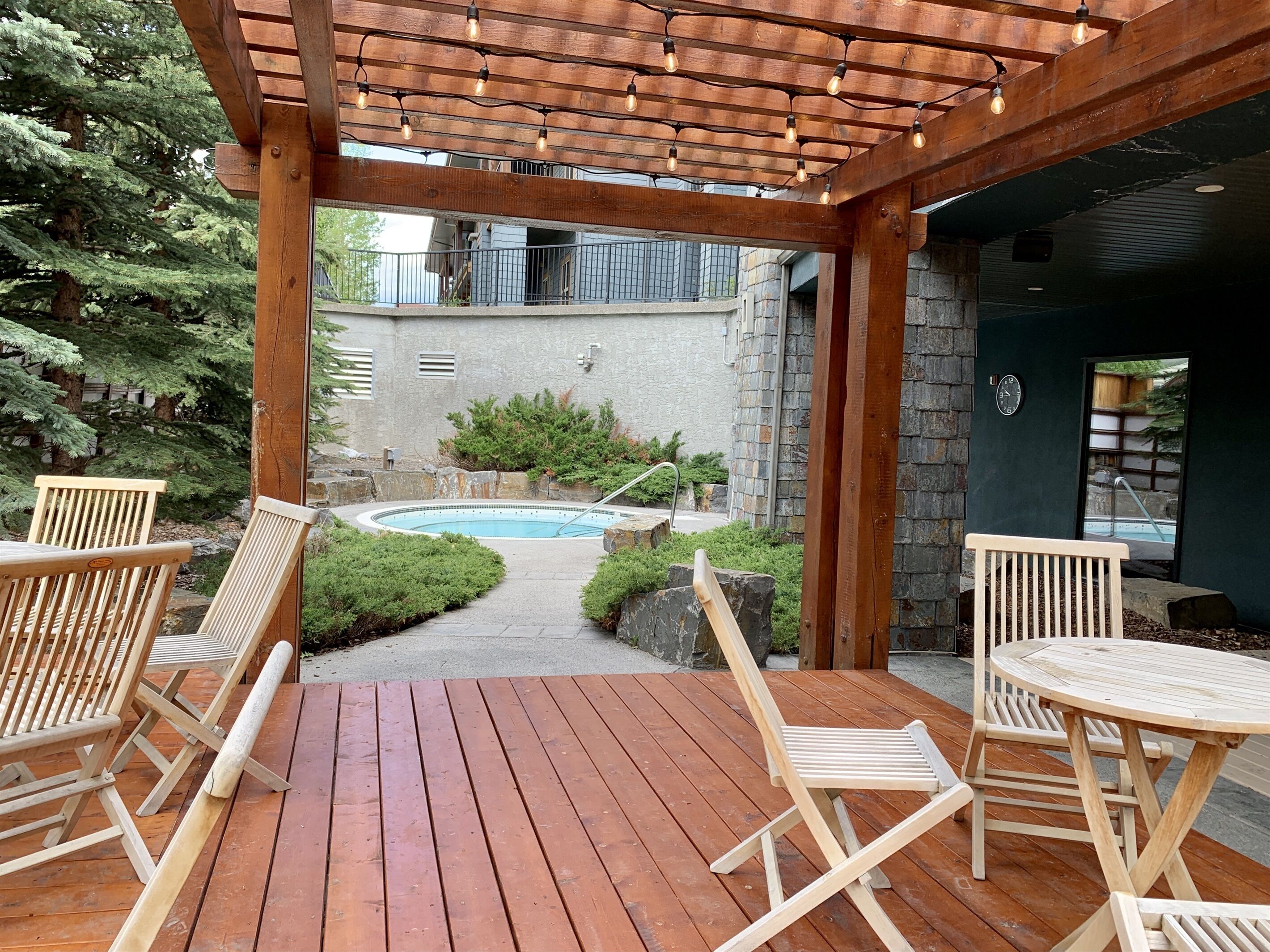 Une terrasse en bois avec des sièges d’extérieur, une piscine et un mur en pierre.