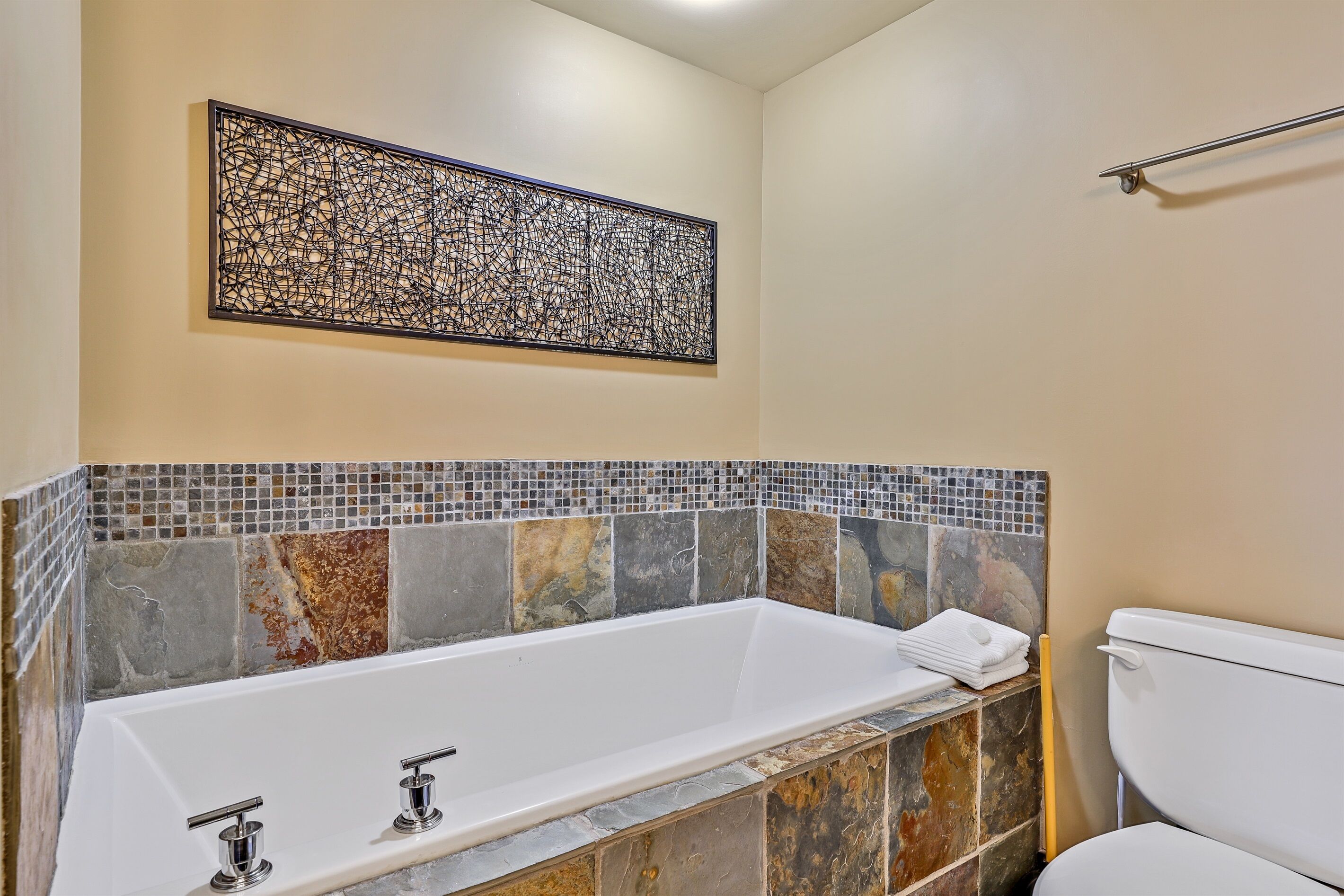 Ein Badezimmer mit einer weißen Badewanne, einem Mosaik-Spritzschutz und einer Toilette.