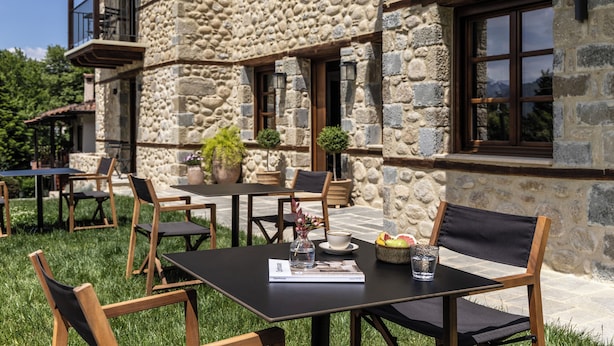 Een terras met stenen muren, houten tafels en stoelen.