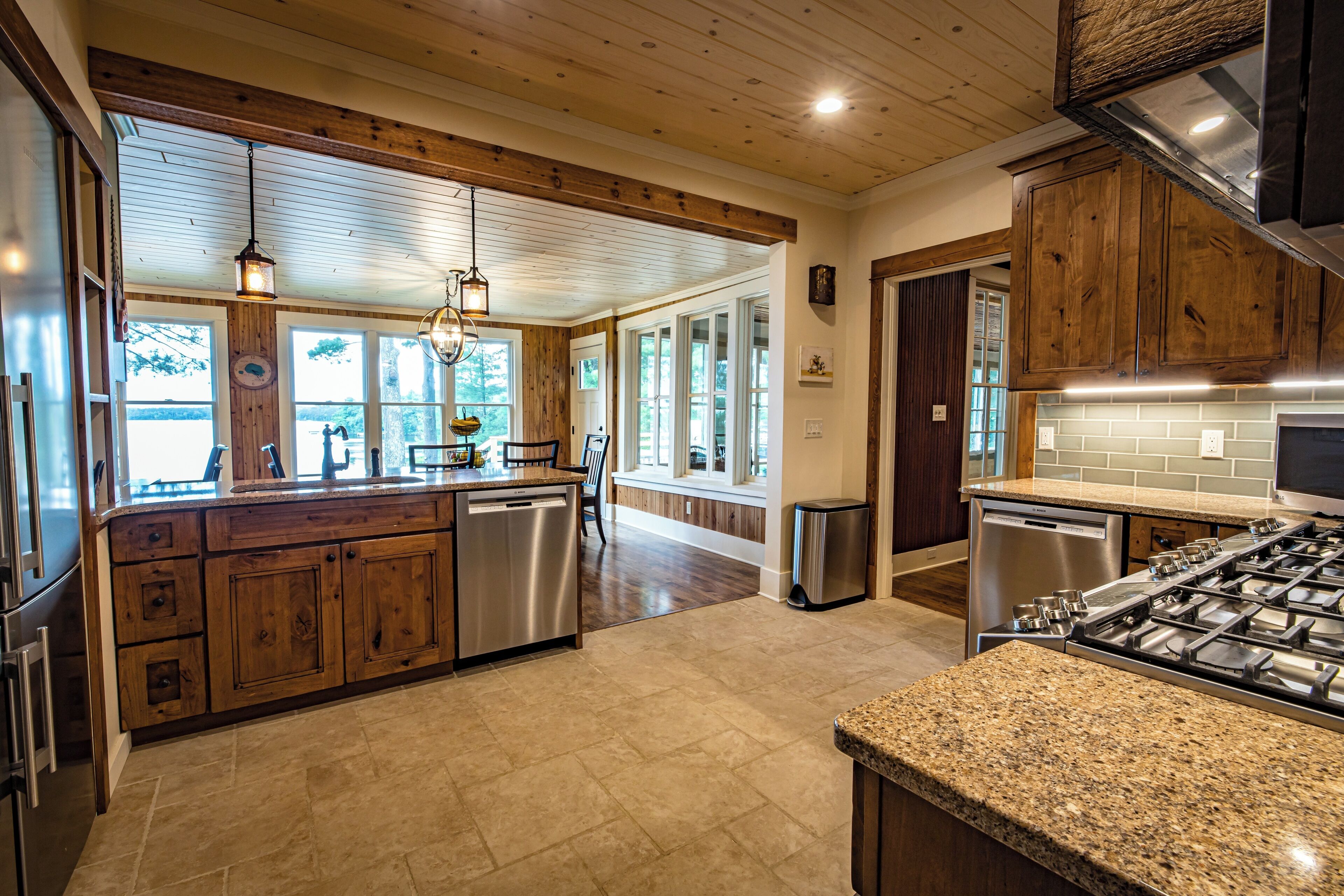 A spacious kitchen with wooden cabinets, a granite countertop, stainless steel appliances, and large windows allowing natural light.