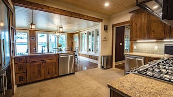 A spacious kitchen with wooden cabinets, a granite countertop, stainless steel appliances, and large windows allowing natural light.