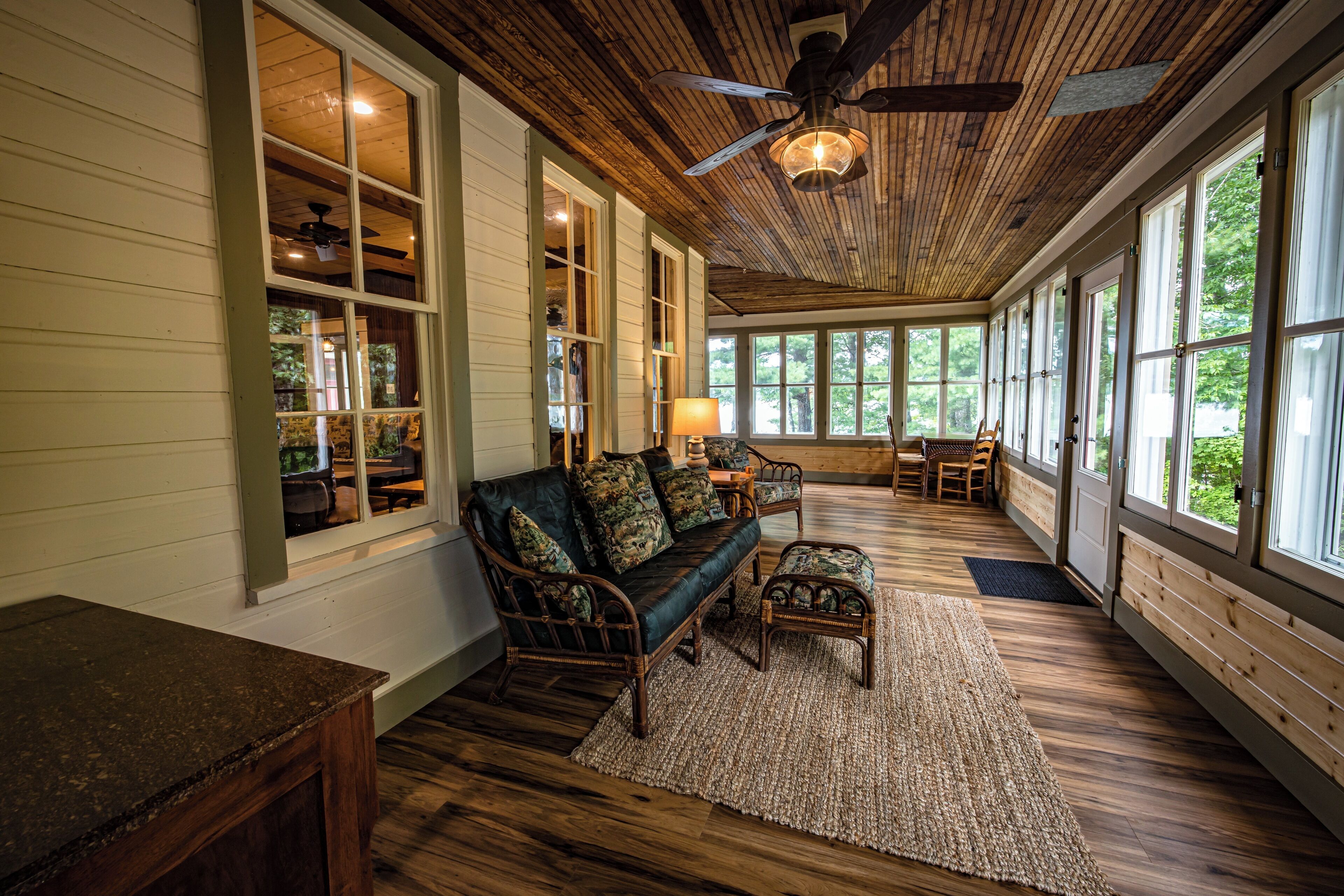 A cozy room with a wooden ceiling, large windows, a sofa, and a table.