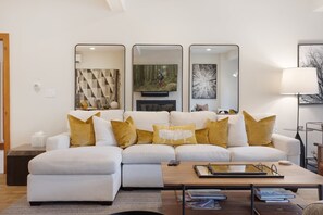 A modern living room with a white sectional sofa, a coffee table, and decorative pillows. There are three mirrors on the wall, a painting, and a lamp. - Charlie's Slopeside: Bachelor Gulch Ski-In/Out, Sleeps 8, Ritz Pool Access + Slopeside Hot Tubs (Avon)