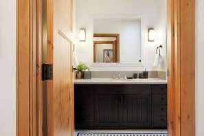 A bathroom with a wooden door, a white sink, a mirror, and a towel rack.