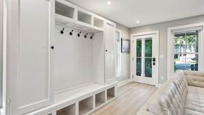 Une pièce moderne et bien éclairée, dotée d’une banquette intégrée et d’un espace pour ranger les manteaux, d’une grande fenêtre donnant sur un paysage verdoyant et d’un canapé moelleux.