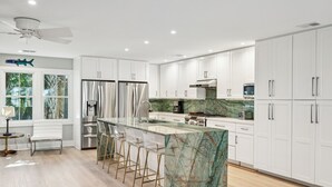Une cuisine moderne avec des armoires blanches, un îlot en marbre, des appareils électroménagers en acier inoxydable et un ventilateur de plafond.