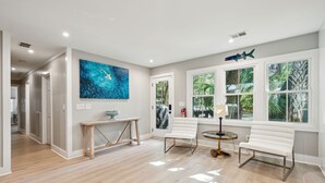 Un salon spacieux avec une grande fenêtre, un banc blanc, une table en bois et un tableau abstrait bleu.