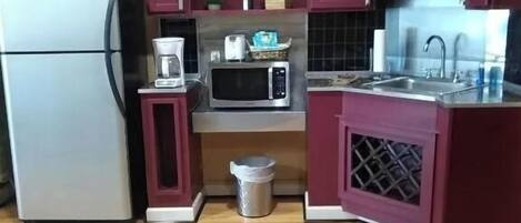 Una cocina compacta con refrigerador, microondas, lavamanos y alacenas.