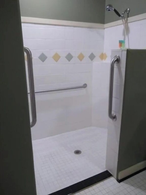 A shower stall with a handrail, a showerhead, and a tiled floor. - Southern Comfort Suites (Mayfield)