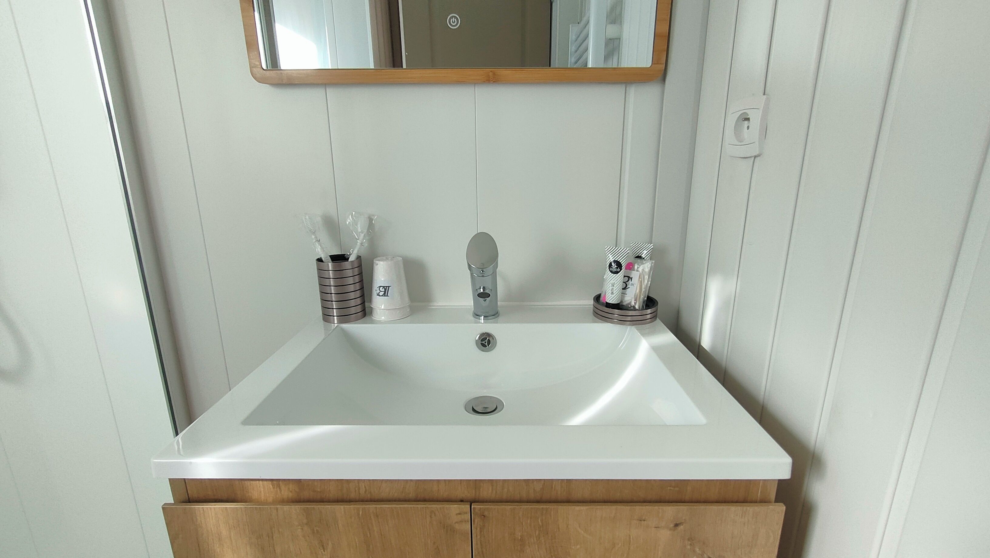 Une salle de bain avec un lavabo blanc, un meuble en bois et un miroir au-dessus du lavabo.