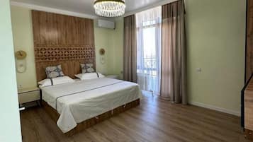Une chambre à coucher avec une tête de lit en bois, un lustre, un lit avec une literie blanche, une table de chevet et une fenêtre avec des rideaux.