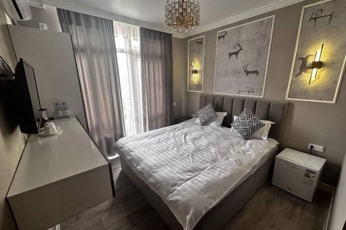 A modern hotel room with a large bed, a bedside table, a TV, and a small bedside cabinet.