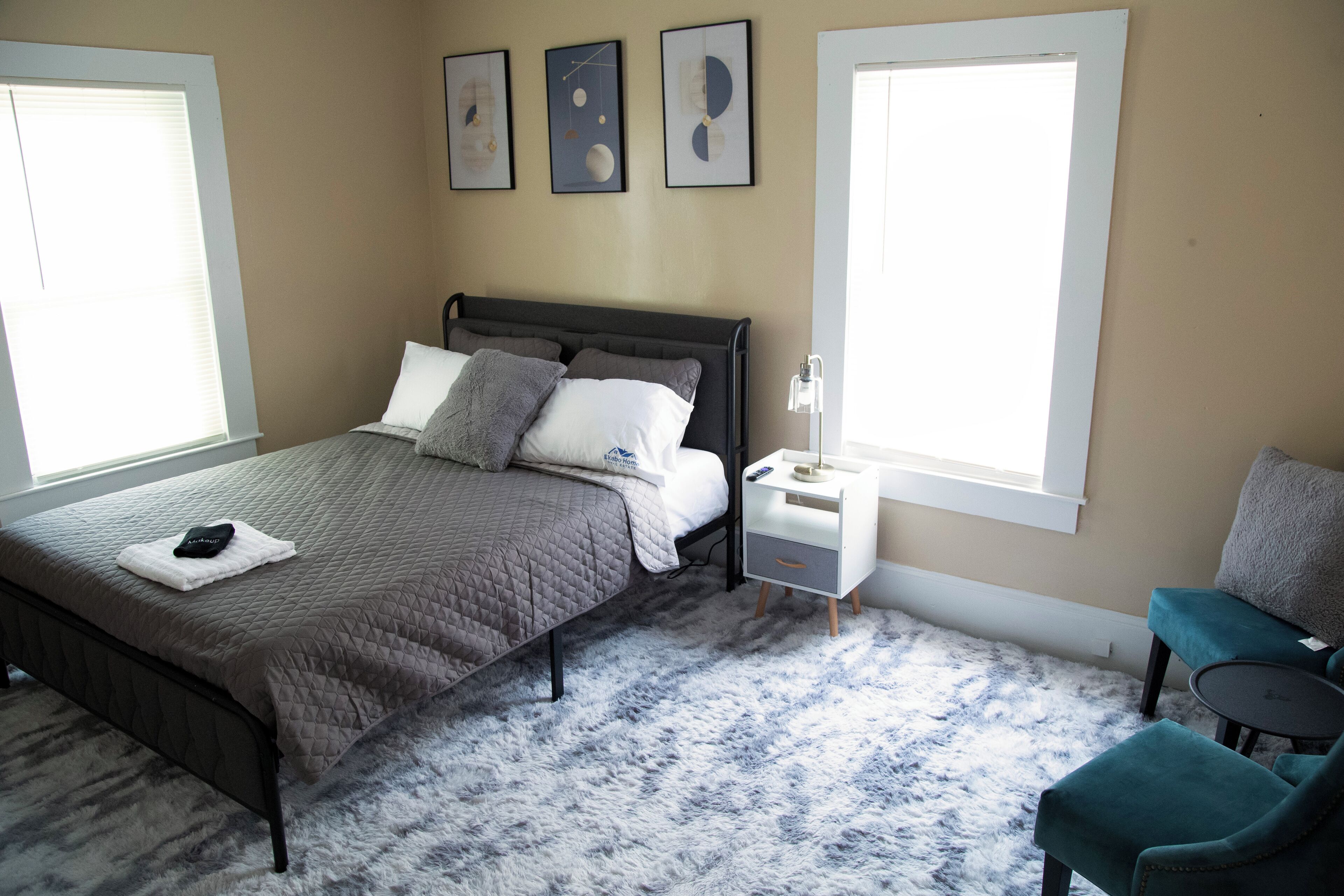 Une chambre à coucher avec un lit, une table de chevet, une chaise et une œuvre d’art accrochée au mur.