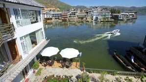 A lakeside hotel with a boat on the water, outdoor seating, and multiple buildings along the shore. - Lanyun Haiwan Inn (Dali City)