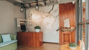 A reception area with a wooden reception desk, a green sofa, a wooden table with chairs, and a decorative wall with branches and flowers. - Lanyun Haiwan Inn (Dali City)