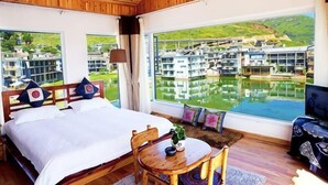 A bedroom with a large bed, a wooden table, and a view of a water body and buildings. - Lanyun Haiwan Inn (Dali City)