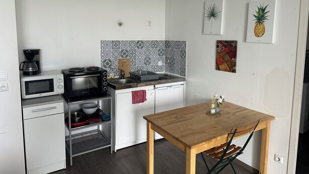 Une cuisine compacte équipée d’un four à micro-ondes, d’une cuisinière et d’un évier, d’un petit four et d’une table en bois avec des chaises.