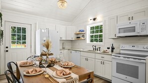 A kitchen with white cabinets, a microwave, a stove, and a dining table set with plates and glasses. - Newly Built Home in Pigeon Forge (Pigeon Forge)