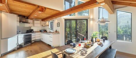 A modern kitchen with wooden beams, large windows, and a dining area with a bench.