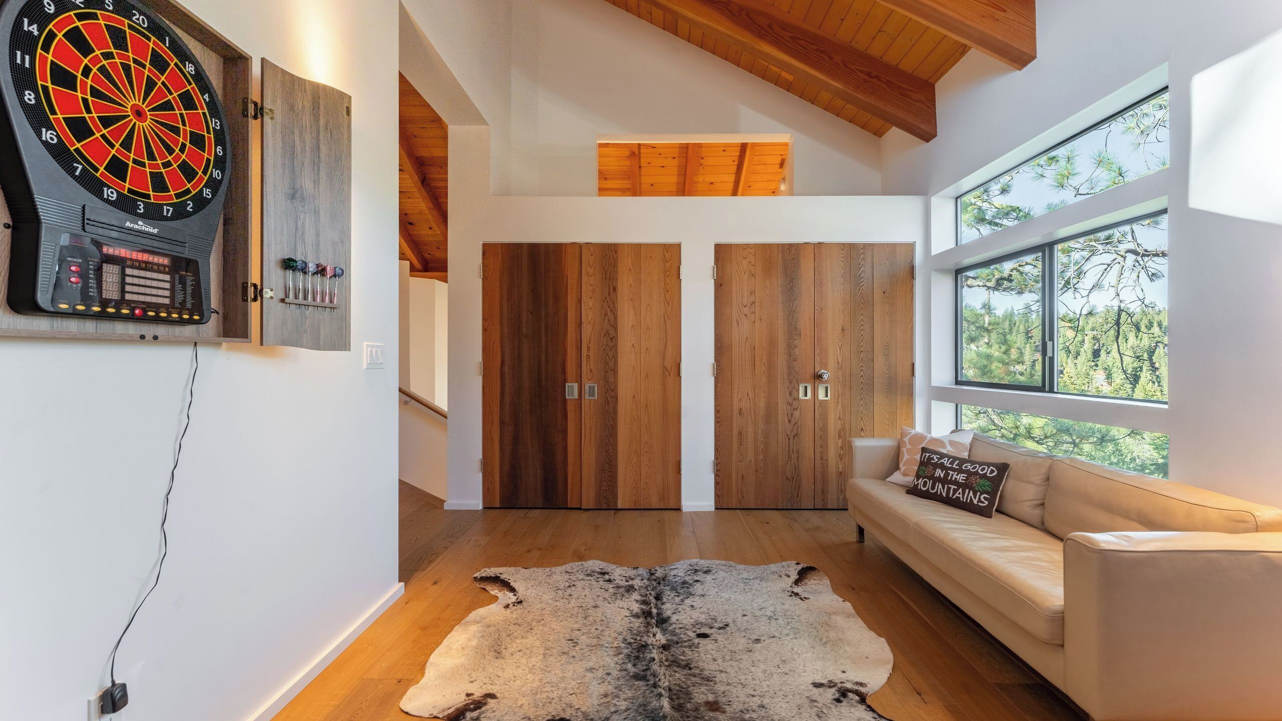 A modern interior with a dartboard, wooden doors, a sofa, and a large window.