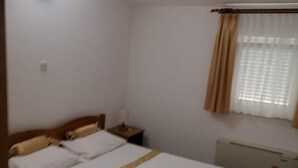 Habitación individual con una cama, cabecera de madera, mesita de noche, radiador y ventana con cortinas.