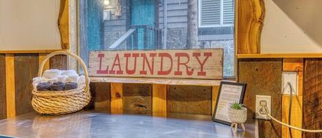 A wooden laundry sign with a basket of towels and a framed certificate on a counter.